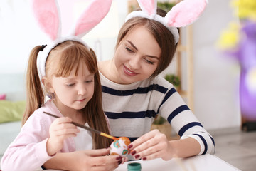 Mother painting Easter eggs with her daughter at table