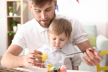 Obraz premium Father painting Easter eggs with his child at table