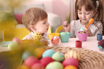 Fototapeta na wymiar Cute kids painting Easter eggs together at table