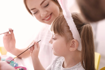 Mother painting Easter eggs with her daughter at table