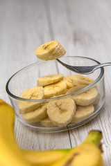 Raw yellow banana fruit slices in a bowl  whit a fork on white wood table