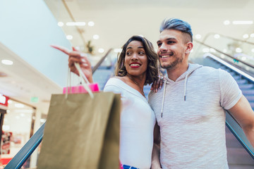 Happy young couple with shopping bags walking in mall - sale, consumerism and people concept