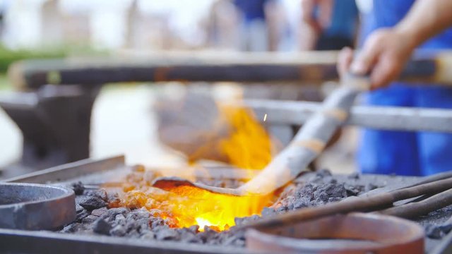 Blacksmith burns hot iron layer for splinter bar 4K. Long shot dolly slide of long iron stick in focus on fire with person in background holding it.