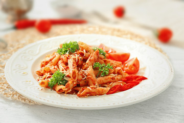 Plate of tasty penne pasta with tomato sauce on table