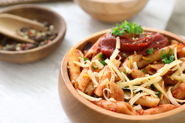 Wooden bowl of tasty penne pasta with tomato sauce on table, closeup