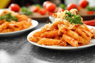Plate with tasty penne pasta and grated cheese on grey table