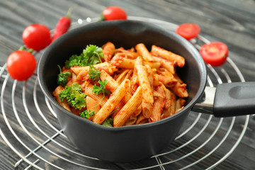 Frying pan with tasty penne pasta and tomato sauce on cooling rack