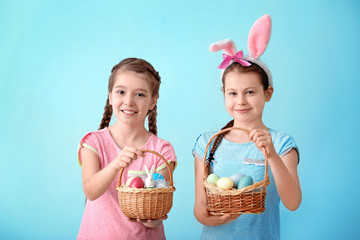 Cute little girls holding wicker baskets with Easter eggs on color background