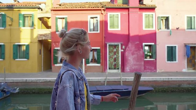 Young woman walking in colorful streets of Burano, Italy during sunset