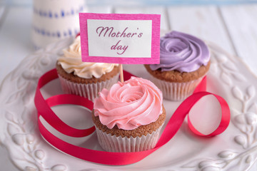 Tasty cupcakes and topper pick with words MOTHER'S DAY on plate