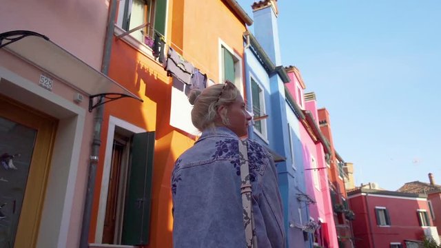 Young woman walking in colorful streets of Burano, Italy during sunset