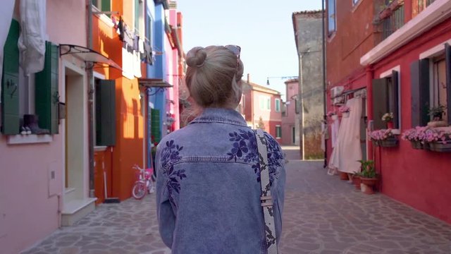 Young woman walking in colorful streets of Burano, Italy during sunset