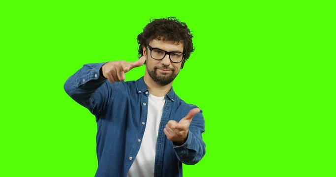Young handsome man in glasses standing in front of the camera and doing gesture like yeah you with both hands. Chroma key. Green screen.