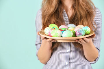 Young woman with plate full of painted Easter eggs on color background, closeup