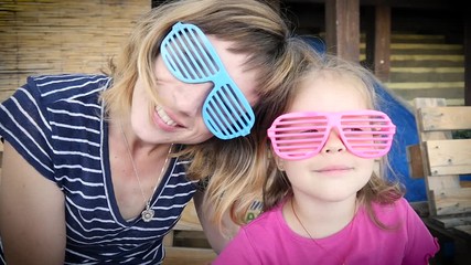 Weekend family amuse mother with child girl portrait in funny glasses sitting smiling slow motion