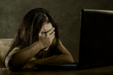 young sad and scared woman covering face with hands stressed and worried looking at laptop computer isolated on grunge background in cyber bullying