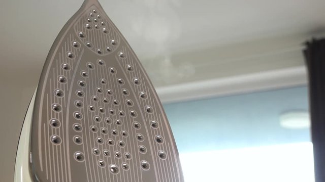 A woman holds an iron and lets steam out of it - closeup