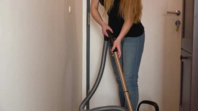 A young attractive woman vacuums a hall in an apartment