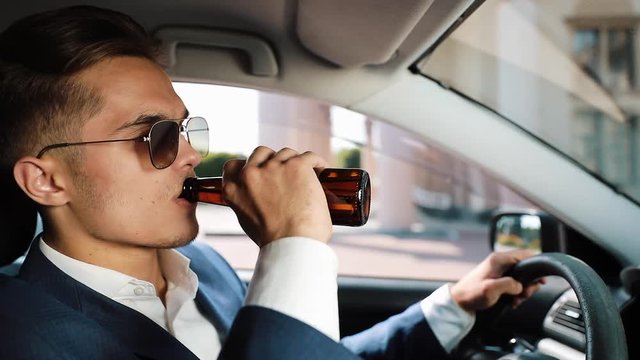 Young businessman drinking beer in car. A man in a bad mood due to a bad deal or a bad news. Drunk, drive and unsuccessful business concept