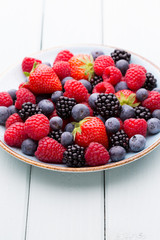 Fresh berry salad on blue dishes. Vintage wooden background.