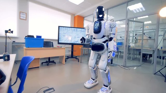A robot stands in a room alone, close up.