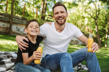 Happy young father sitting with his little son outdoors drinking juice.