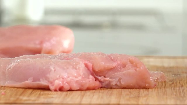 A woman pounds a chicken breast on a chopping board in a kitchen - closeup