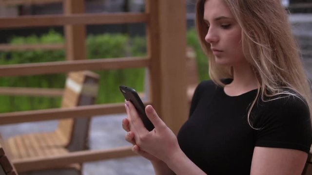 portrait young businesswoman sitting on the bench at the open air using smartphone. attractive millennial texting message or checking email