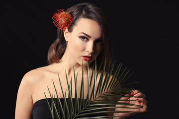 Portrait of young woman with beautiful professional makeup and palm leaf on dark background