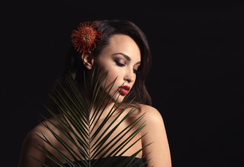 Portrait of young woman with beautiful professional makeup and palm leaf on dark background