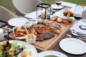 Meat platter served with salad, fries and red wine with three choice of sauce on wood block at fine dining table set.
