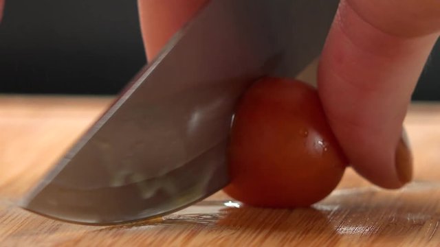 A woman cuts cherry tomatoes with a knife at a kitchen counter - closeup