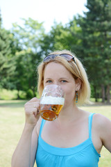 Portrait of happy woman holding glass of beer outside on sunny day.