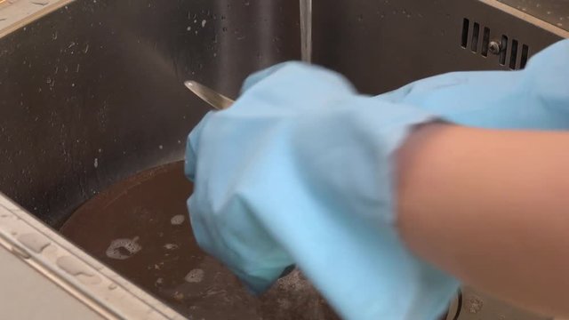 A woman does dishes with a sponge in a sink - closeup
