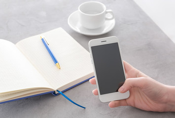 Woman holding smartphone with blank screen at table
