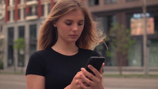 young business woman standing on the street using smartphone. attractive female with long blond hair texting message or checking email or chatting with friend outdoors