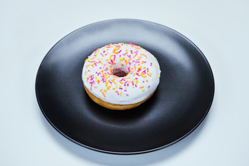 Appetizing donut with sprinkles lie on a black ceramic plate.