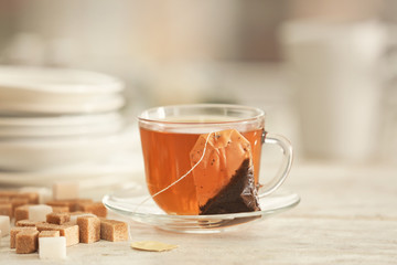 Saucer with cup of hot beverage and tea bag on table