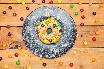 Appetizing golden donut lie on ceramic plate, sprinkled with colorful chocolate pellets.