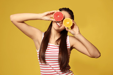 Funny young woman with citrus fruits on color background