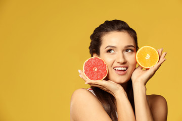 Beautiful young woman with citrus fruits on color background