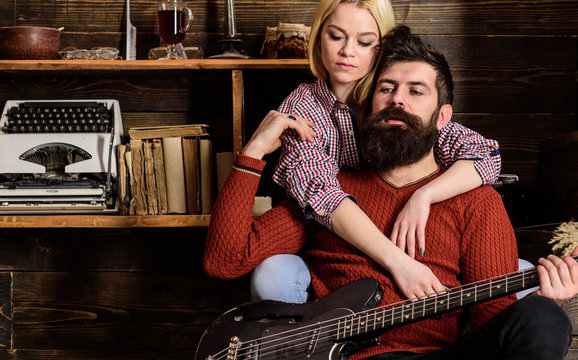 Lady and man with beard on dreamy faces hugs and plays guitar. Couple in wooden vintage interior enjoy guitar music. Couple in love spend romantic evening in warm atmosphere. Romantic evening concept