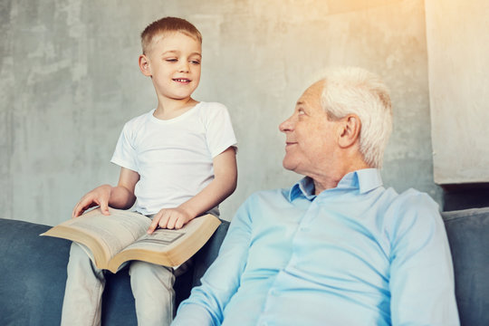 New facts. Curious clever little boy showing a big picture in a book to his attentive loving senior grandfather