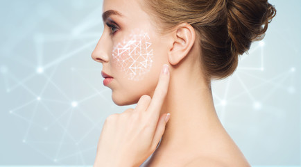 beauty, technology and people concept - beautiful young woman pointing finger to her skin over blue background with low poly shape projection on cheek