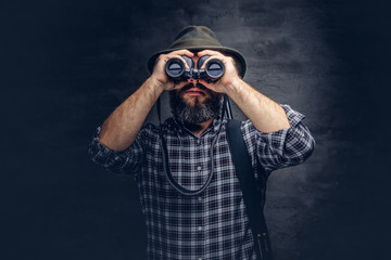Portrait of a bearded hunter traveler tries to find prey while looking through binoculars.