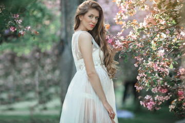 Pregnant pretty woman is wearing white fashion dress posing in pink apple garden, summer time