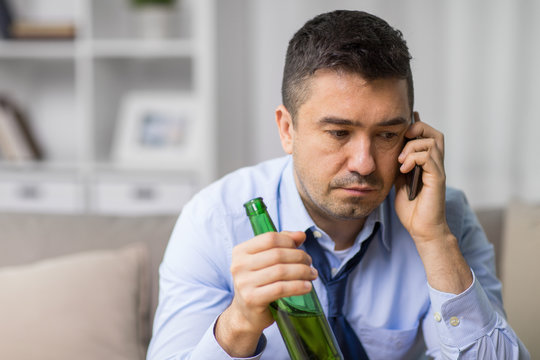 alcoholism, alcohol addiction and people concept - male alcoholic drinking beer and calling on smartphone at home
