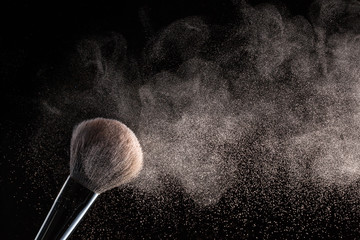 Brush for makeup with flying around powder is isolated on a black background