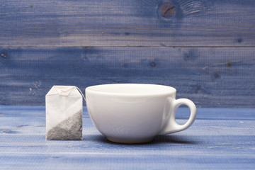 Tea time concept. Cup or white porcelain mug with transparent hot water and bag of tea. Mug filled with boiling water and teabag on blue wooden background. Process of tea brewing in ceramic mug