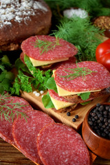 Sandwich with salami, cheese and arugula salad surrounded by the ingredients